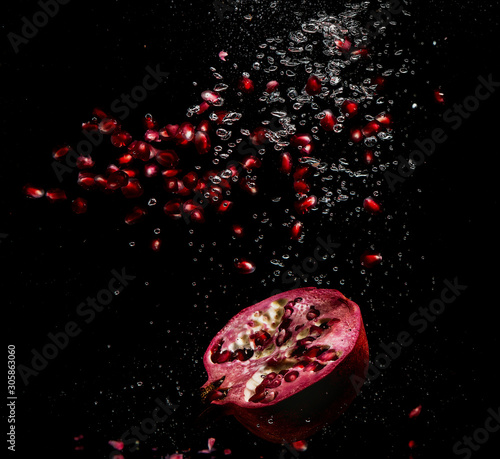 Juicy pomegranate with grains on a black background with splashes of water and air bubbles