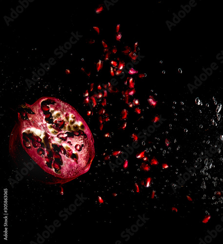 Juicy pomegranate with grains on a black background with splashes of water and air bubbles