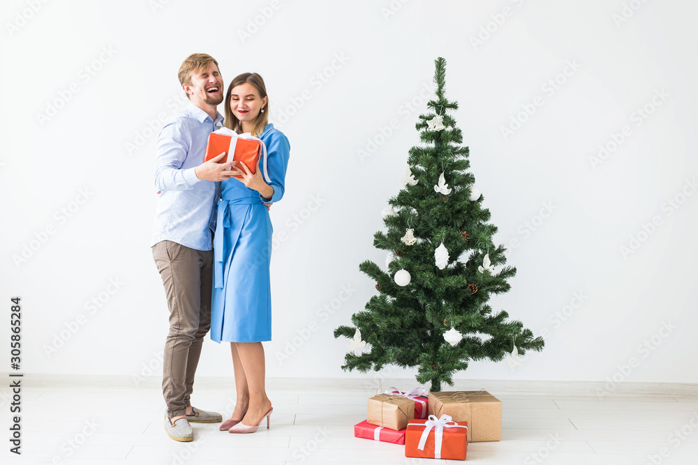 Holidays and festive concept - Young happy couple near a Christmas tree on white background Holidays and festive concept - Young happy couple near a Christmas tree on white background