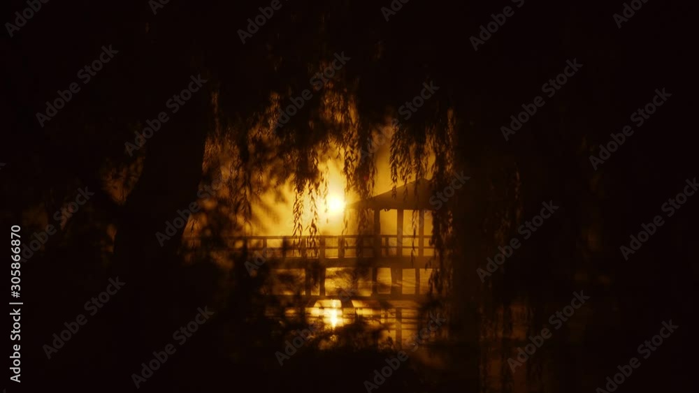 City park at night. A small house in japanese style on the bridge. A lamp light is orange and mysterious. Mystic place with wonderful atmosphere City park at night. A small house in japanese style on the bridge. A lamp light is orange and mysterious. Mystic place with wonderful atmosphere
