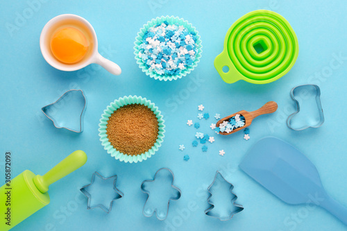 ingredients and kitchen tools for baking with cookies cutter on blue background, flat lay