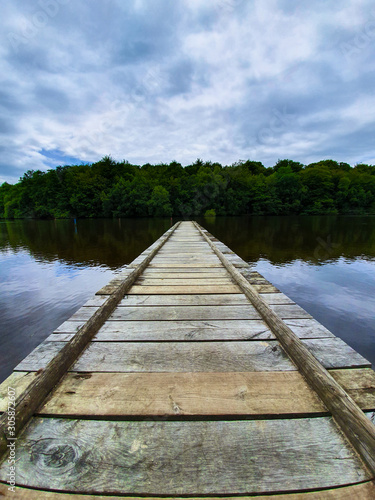 Long wooden walking pier on a lake in Fougeres, Brittany, France. Calm and still waters in the countryside.