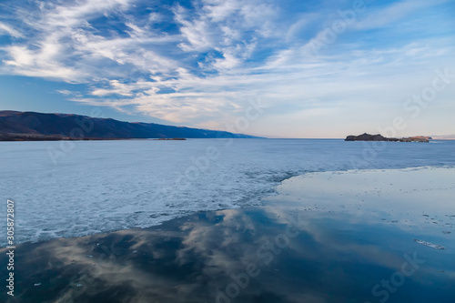 Baikal lake in may with cracking ice  water and reflection of blue sky with clouds