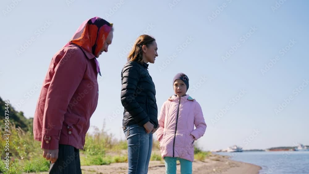 An elderly woman with an adult daughter and granddaughter walk along the shore, talking joyfully and laughing on an autumn day. A young woman spends time with an elderly mother and daughter. An elderly woman with an adult daughter and granddaughter walk along the shore, talking joyfully and laughing on an autumn day. A young woman spends time with an elderly mother and daughter.