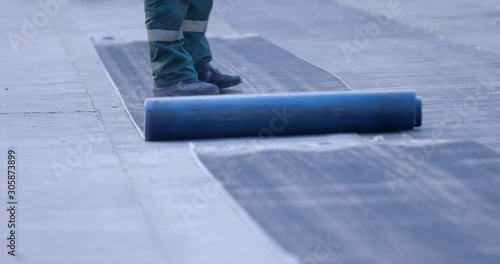 A worker unwinds a roll of ruberoid on a surface that needs to be isolated from water
