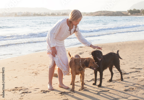 Blonde girl with a dogs playing in the morning on the beach © artmim