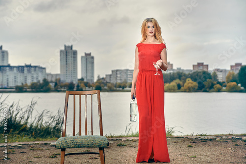 beautiful girl in evening red dress on the lake with a glass and a bottle of wine