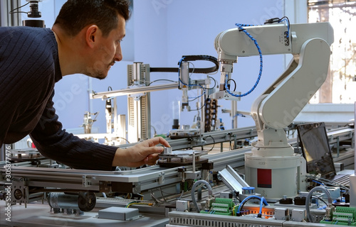 industry 4.0 concept: A mechatronics engineer is holding product and teaching robot arm the positions with teach pendant on smart factory production line background. Selective Focus. photo