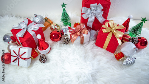 Christmas decoration on white hairy carpet. Gift box with ribbon, glossy ball, pine cone, Christmas tree and mini santa hat on fluffy rug. Present and decorative objects for New Year holiday