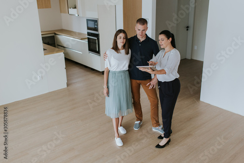 Estate agent with digital tablet showing young couple new apartment