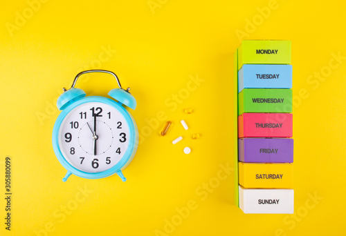 Foto Blue alarm clock, pills and a multicolored weekly pill organizer as the Time to