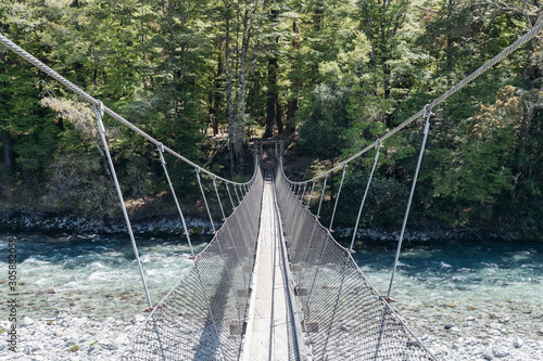 Swing bridge crosses clear river into native New Zealand bush