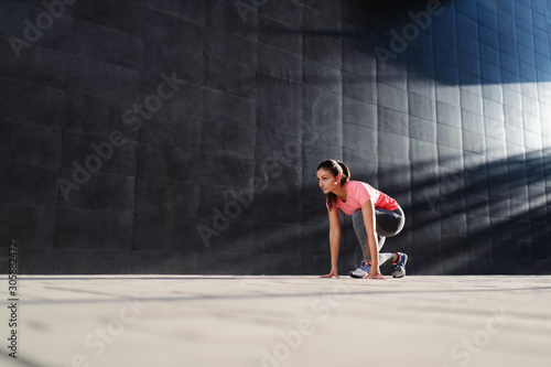 Beautiful fit caucasian brunette in sportswear kneeling and preparing to run. Back lit.
