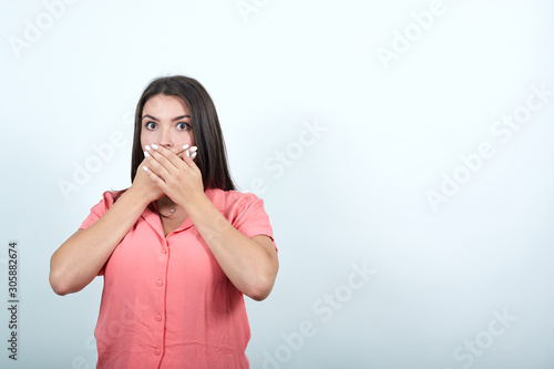 Shocked caucasian young woman in pink shirt keeping hands on mouth, looking scared isolated on white background in studio. People sincere emotions, lifestyle concept.