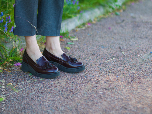 Stylish woman in gray trousers and brown leather shoes (loafers), in a white shirt and a leather jacket