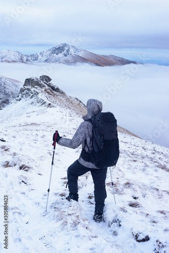 Tourist stands on hiking trail in winter mountains with black backpack photo