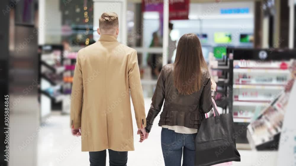 Backside view, man and woman go shopping holding hands, steadicam shot Backside view, man and woman go shopping holding hands, steadicam shot