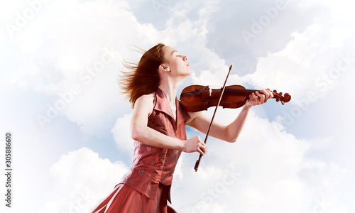 Canvas Print Woman violinist in red dress playing melody against cloudy sky