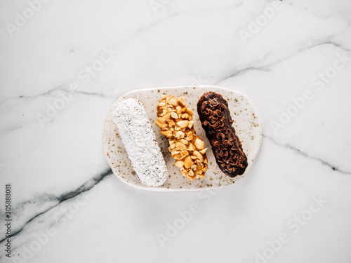 Set of three homemade eclairs on marble background. Close up view of delicious healthy profitroles with different decor elements - chocolate, peanut and sherdded coconut. Vertical. photo