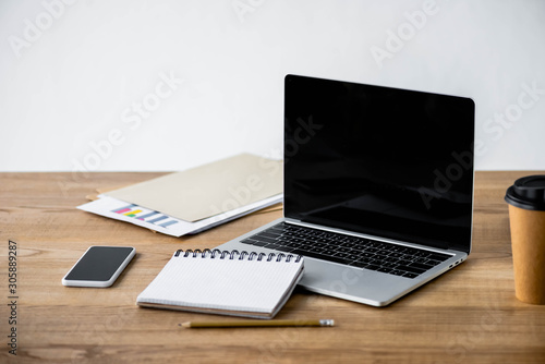 laptop, smartphone, notebook, pencil, paper cup and folder on wooden table