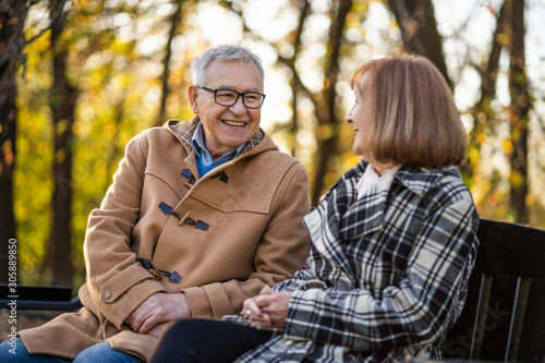 Senior couple is sitting on bench in park and enjoying autumn.