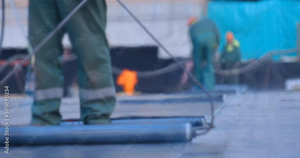 The workers heats the roll of ruberoid with the flame of a gas burner and firmly connect with a surface of stadium main field that needs to be isolated from water The workers heats the roll of ruberoid with the flame of a gas burner and firmly connect with a surface of stadium main field that needs to be isolated from water