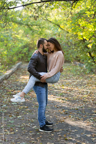 Young beautiful couple in the Park. A man holds a woman in his arms. In the background autumn forest. © jonnyslav