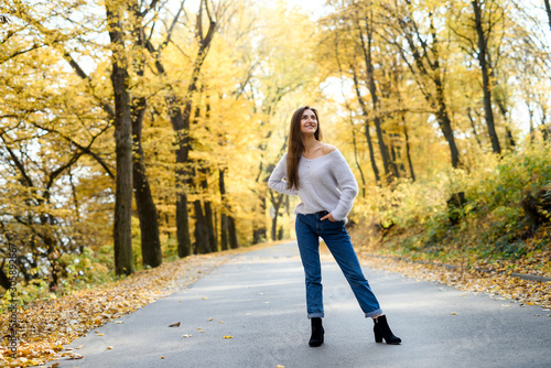 Portrait of brunette woman in casual wear in autumn park. Yellow colours around beautiful woman © RomanR