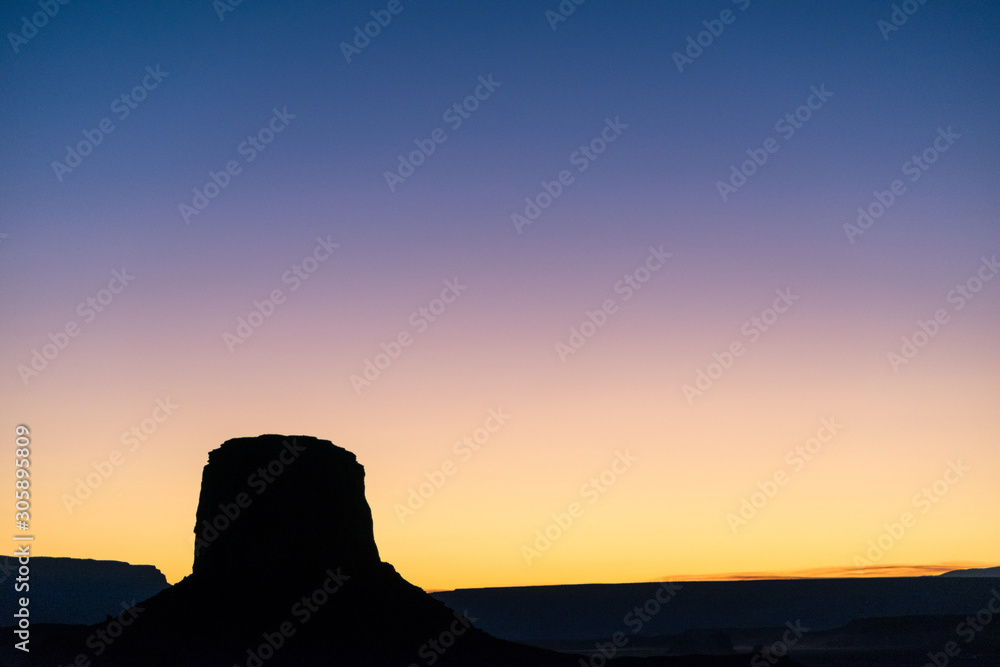 Sunset hues over the silhouette of a butte in Monument Valley