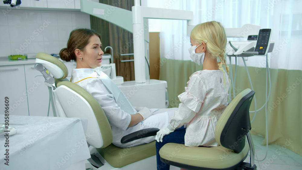 Dentist sits in patient chair and talks with girl Dentist sits in patient chair and talks with girl