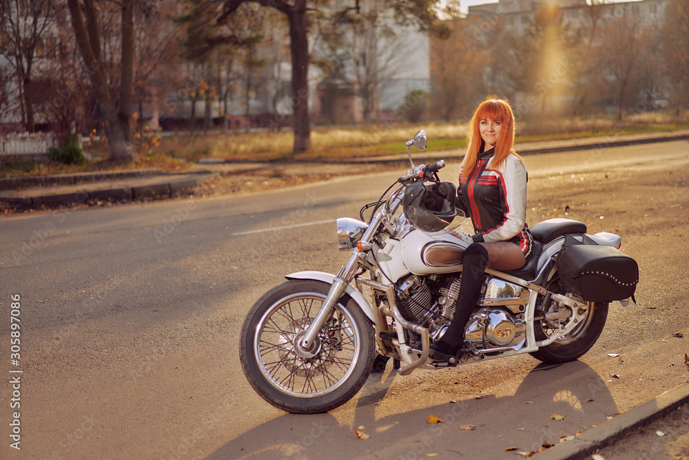 white motorcycle tourer and woman biker on the road in the autumn city at sunset