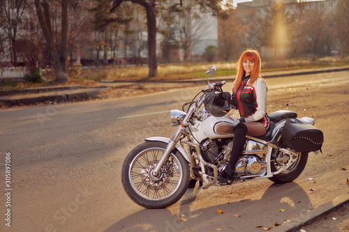 white motorcycle tourer and woman biker on the road in the autumn city at sunset photo