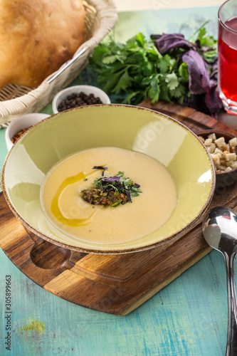 Fresh homemade vegetable cream soup with croutons in green bowl on cutting board on blue wooden table