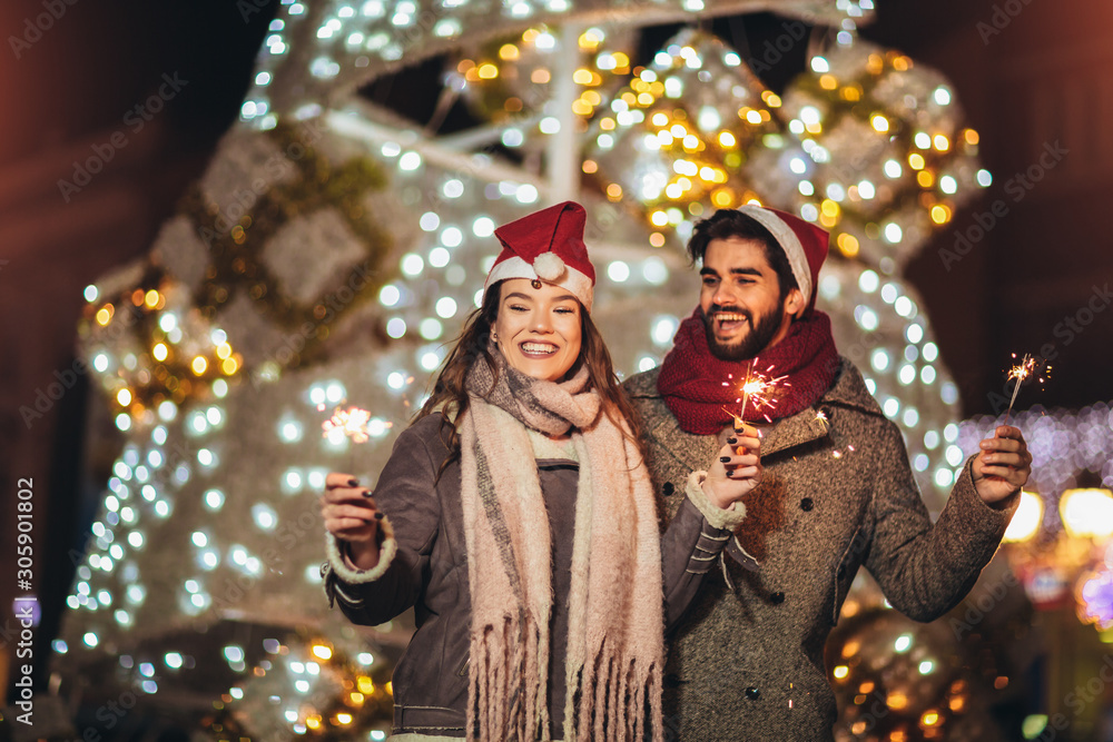 Young loving couple burning sparklers by holiday illumination on new years eve.