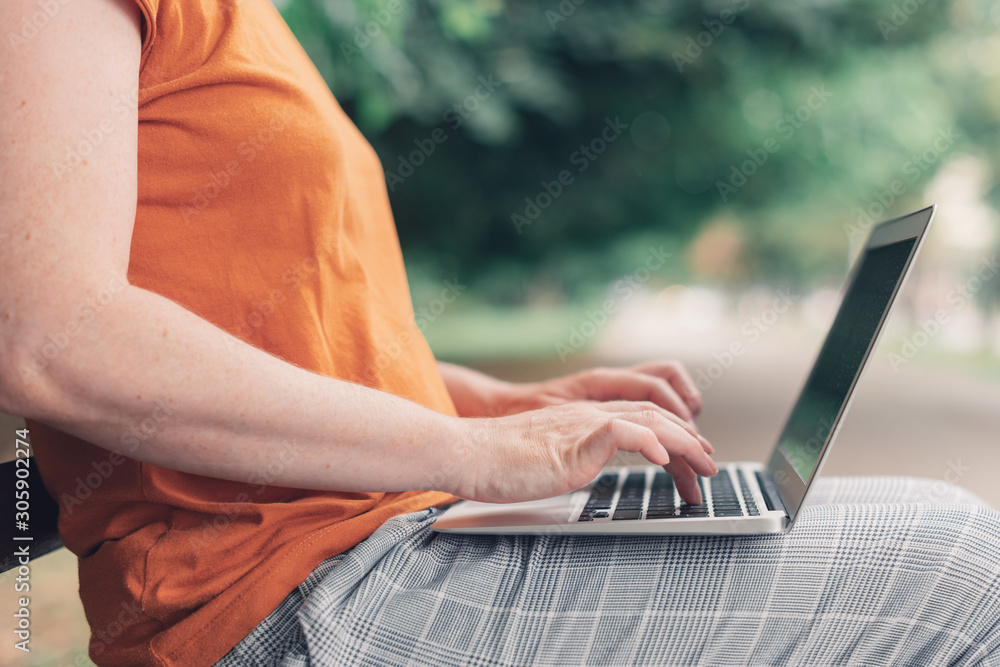 Naklejka premium Woman using laptop computer on park bench