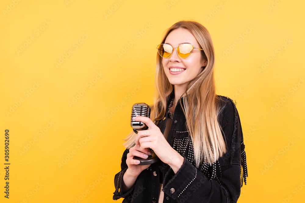 Beautiful young woman in glasses and with microphone on yellow background Beautiful young woman in glasses and with microphone on yellow background