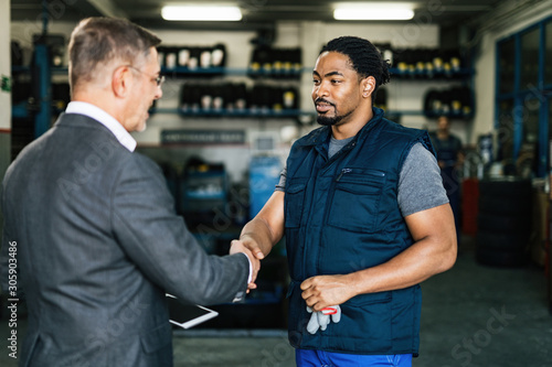 Smiling African American car mechanic handshaking with customer in a workshop.