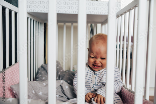 Photography baby girl with blue eyes and blond hair is crying in her bed