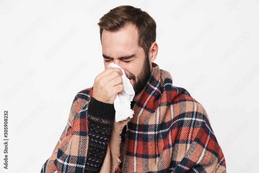 Portrait of ill guy wrapped in blanket sneezing and holding paper napkin Portrait of ill guy wrapped in blanket sneezing and holding paper napkin