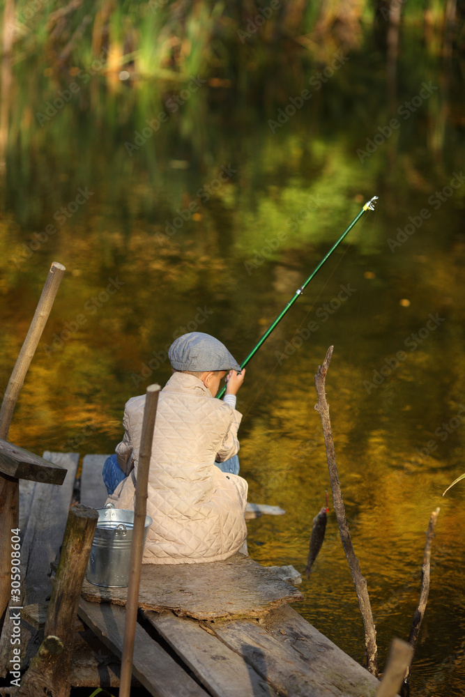 Kid fishing in a river, sitting on a wood pontoon Kid fishing in a river, sitting on a wood pontoon