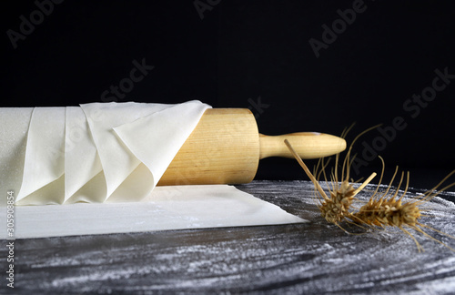 Primo piano di pasta fillo su un tavolo infarinato. Sfondo scuro con mattarello e spighe di grano.