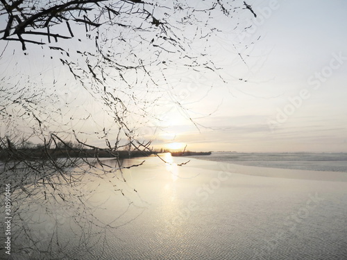 The mixed image of the view of the ice on the surface of the lake and the natural background of the view of the lake shore at the cold spring day at the City Park. 