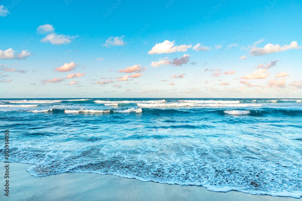 Fototapeta premium Waves on the beach at sunset, pink and turquoise cloudy sky