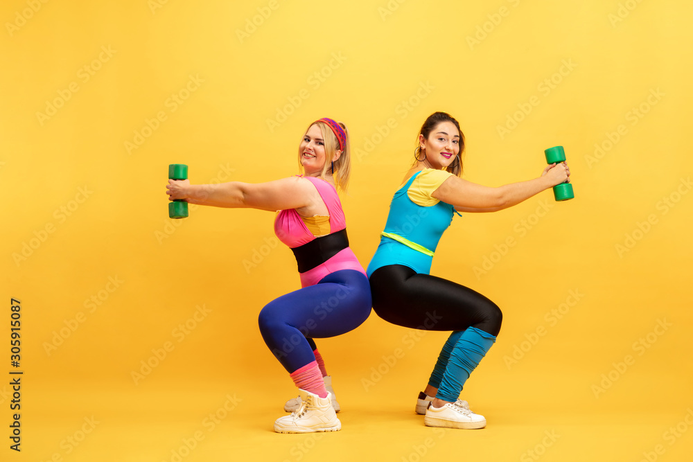 Young caucasian plus size female models training on yellow background. Copyspace. Concept of sport, healthy lifestyle, body positive, fashion. Friendship, girl power. Stylish woman practicing, smiling Young caucasian plus size female models training on yellow background. Copyspace. Concept of sport, healthy lifestyle, body positive, fashion. Friendship, girl power. Stylish woman practicing, smiling