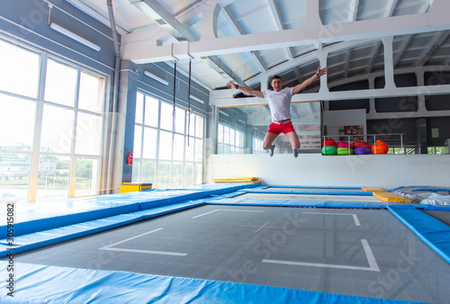 Fitness, fun, leisure and sport activity concept - Handsome happy man jumping on a trampoline indoors