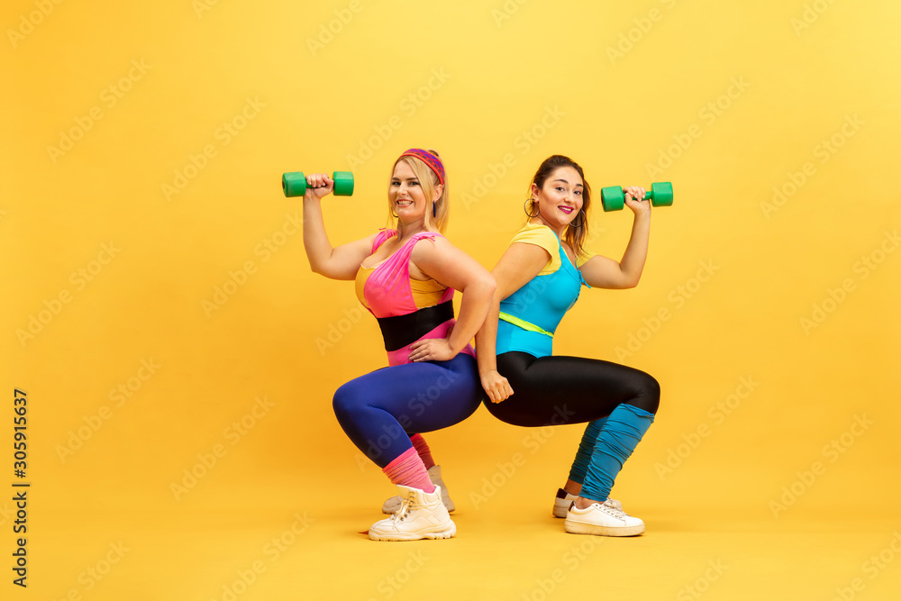 Young caucasian plus size female models training on yellow background. Copyspace. Concept of sport, healthy lifestyle, body positive, fashion. Friendship, girl power. Stylish woman practicing, smiling Young caucasian plus size female models training on yellow background. Copyspace. Concept of sport, healthy lifestyle, body positive, fashion. Friendship, girl power. Stylish woman practicing, smiling
