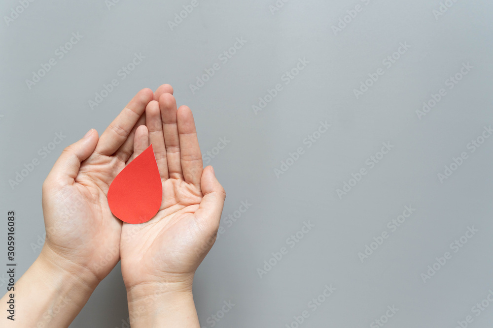 Naklejka premium Blood donation - Human hand holding blood drop symbol on gray background with copy space. World blood donor day and save life concept. Flat lay.