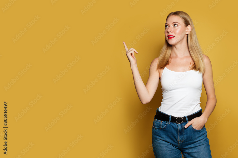 Young pretty woman pointing up on bright yellow background