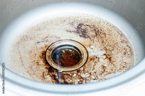 The drain of the stainless steel sink for washing dishes is clogged with water and food particles.