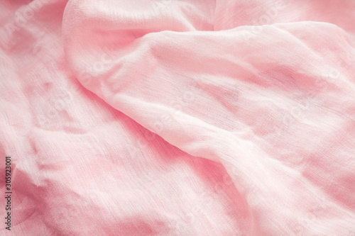 Textural background from a light cotton natural fabric of a pale pinkish-orange hue. Wavy folds of lightweight fabric.